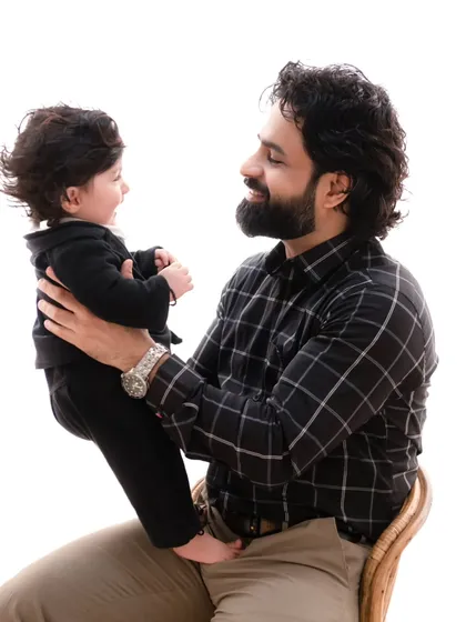 A sweet, interactive moment between father and son. The minimalist setting allows their smiles and the baby's happy expression to be the focus.