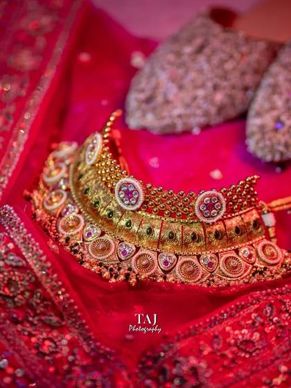 A classic detail shot of the bride's essentials. The rich gold of the necklace and the sparkle of the shoes are laid out on the vibrant red lehenga, capturing the elegance of the bridal attire.
