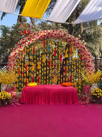 A beautiful Haldi seating area with a backdrop of hanging floral strings. The vibrant pink stage and colorful floral arrangements create a joyful and picturesque setting.