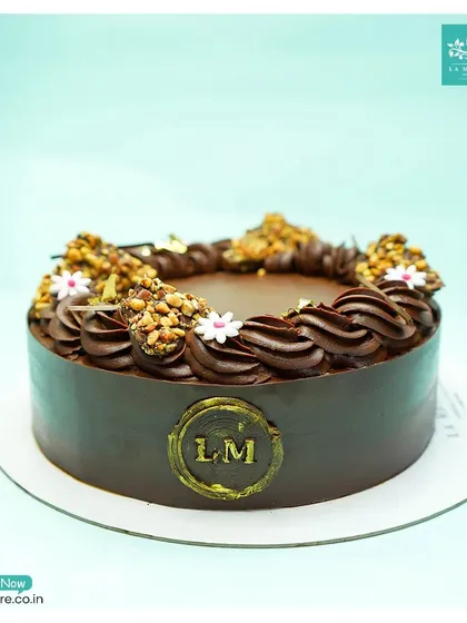 A beautifully crafted chocolate cake, finished with our signature gold 'LM' seal. The top is adorned with chocolate piping and crunchy nut clusters.