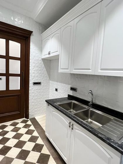 The combination of a classic checkerboard floor, white tiled backsplash, and a rich wooden door gives this kitchen a unique and timeless character.