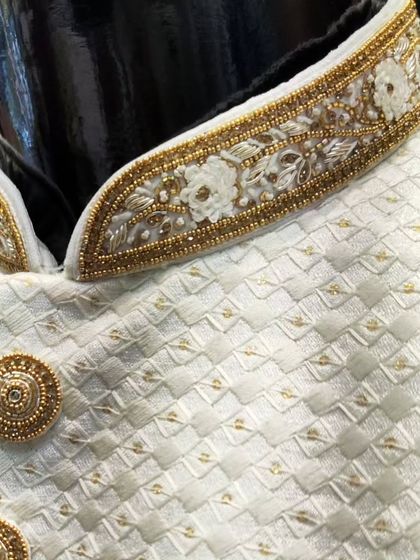 A detailed view of the craftsmanship on a white sherwani. Notice the hand-embroidered floral motifs on the collar and the custom-designed textured gold buttons.