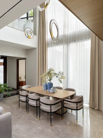 This dining area is situated in a stunning double-volume space, with dramatic pendant lights that draw the eye upward. The neutral color palette and clean lines of the furniture create a feeling of serene, modern elegance.