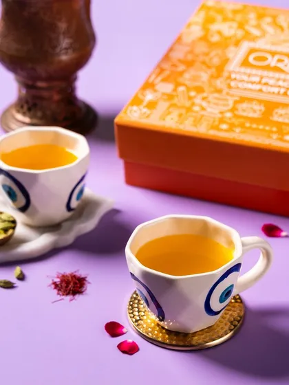 Saffron-infused tea in artistic mugs, shot for Orika Spices. The styling with saffron strands and rose petals highlights the product's premium ingredients.