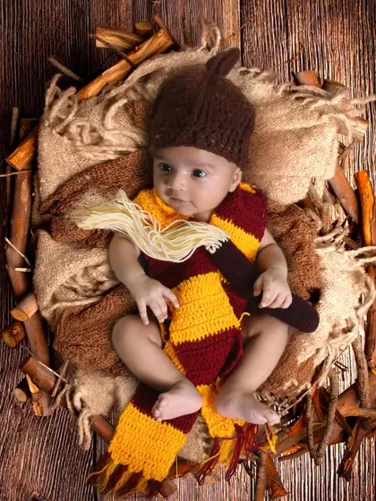A newborn dressed in a Harry Potter scarf and hat, ready for their journey to Hogwarts.
