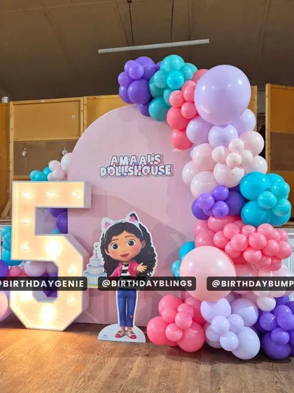 A colorful Gabby's Dollhouse theme for a fifth birthday, featuring a character cutout, a light-up number '5', and a vibrant balloon arch.