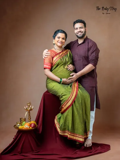 A beautiful couple's portrait from a traditional shoot. The husband stands supportively behind his wife, who is seated, creating a classic composition that highlights their partnership on this journey.