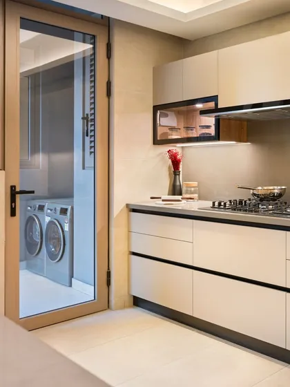 This kitchen layout thoughtfully includes a utility area, neatly tucked away behind a glass door. This keeps appliances like the washing machine out of sight while still being easily accessible, maintaining the kitchen's uncluttered aesthetic.