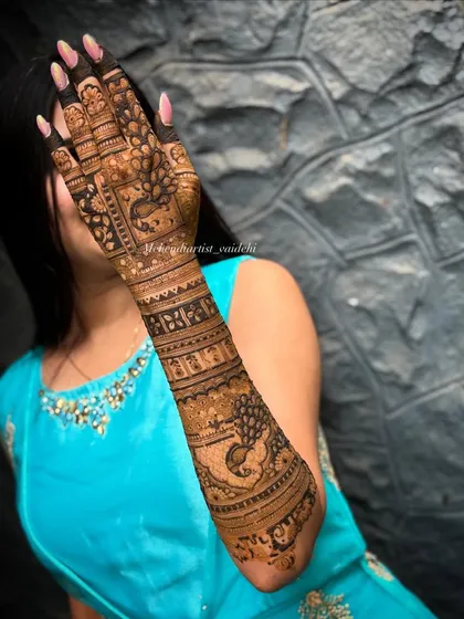 A stunning full-arm mehendi for an engagement bride. The design incorporates bold peacock figures, a classic symbol of grace and beauty in Indian culture, combined with intricate geometric bands for a balanced and striking look.