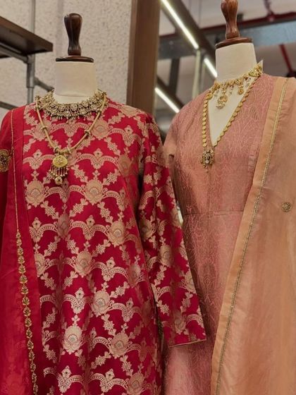A display of classic Banarasi brocade suits by Raw Mango, one in royal red and the other in soft peach, styled with statement jewelry.