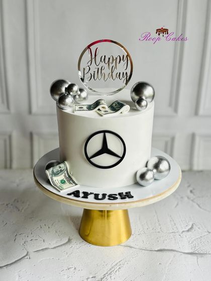 A classy cake for a classy celebration. This Mercedes-themed birthday cake features the iconic logo, edible dollar bills, and silver spheres for a touch of luxury.
