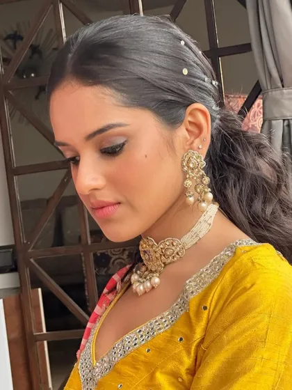 A close-up of the Haldi look, showing the soft makeup and the beautiful detail of her jewelry. The look is designed to enhance her natural features.