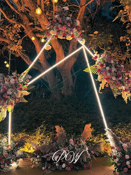 A modern, geometric arch decorated with florals and neon lights serves as a unique photo point for an outdoor evening event.