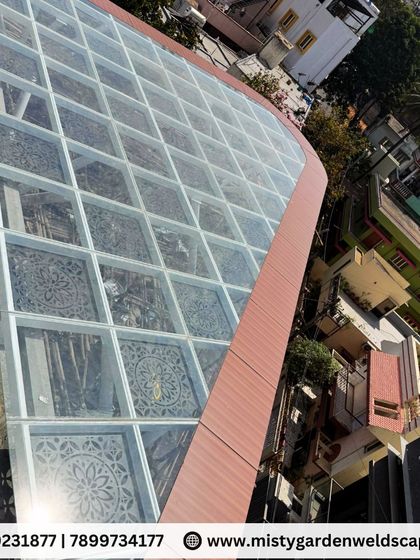 An aerial view of the large, curved glass pergola during installation. This perspective showcases the scale and complexity of the project, which was custom-designed to fit the building's unique shape.