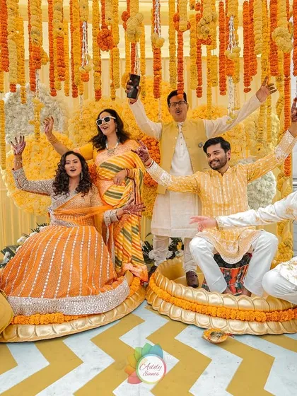 A fun group photo from the Haldi ceremony, with the couple and their friends posing joyfully against the vibrant marigold backdrop.