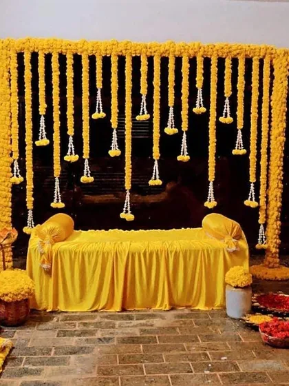 This is a beautiful and traditional Haldi seating arrangement. I created a backdrop entirely of marigold strings with jasmine tassels, which looks stunning against the yellow seating.