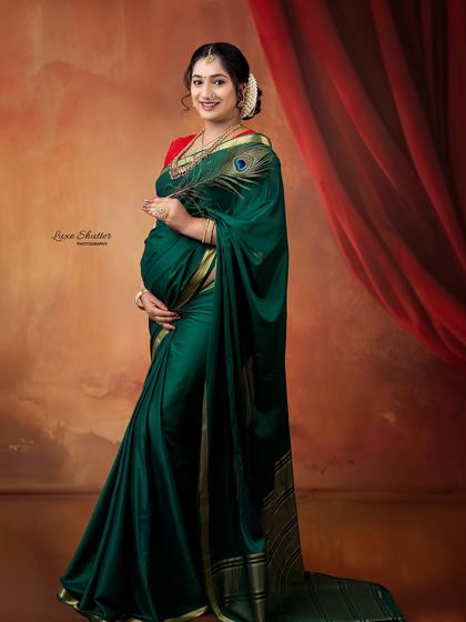 A joyful portrait of the mother-to-be in a stunning green saree, holding a peacock feather. The rich colors and traditional styling make this a vibrant and beautiful image.