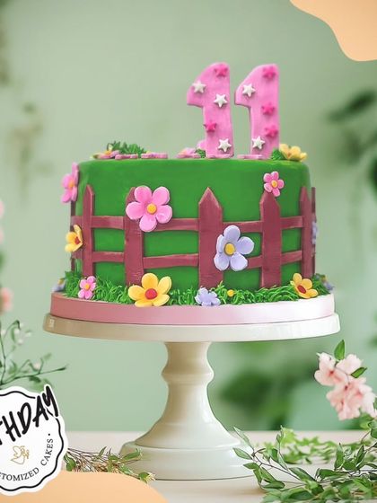 A sweet garden fence cake for an 11th birthday. The design features a charming fence, green grass, and colorful fondant flowers for a playful and pretty look.