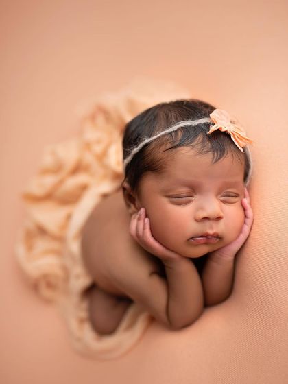 A wider view of the froggy pose, showing the baby's full form against a soft peach background.