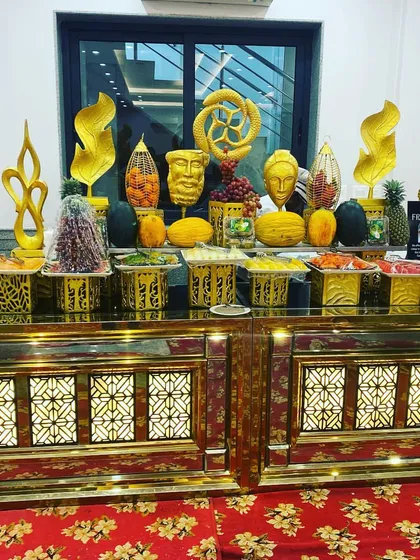 Our exotic fresh fruit station, a healthy and visually appealing addition to any buffet. The counter features an array of local and imported fruits, artfully carved and displayed on ornate gold stands and sculptures.