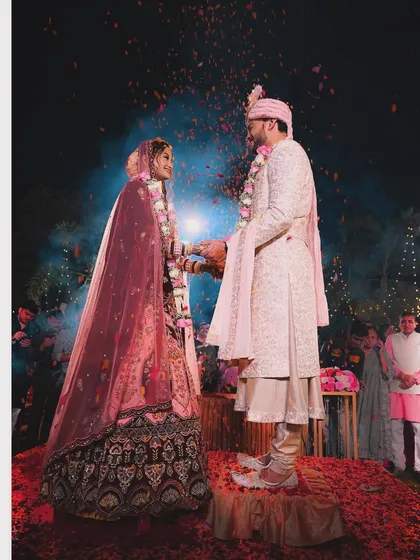 The Varmala ceremony, a pivotal moment in a Hindu wedding, captured with a shower of petals. The dramatic lighting and action make this a stunning, cinematic shot.