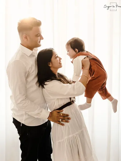 A light-filled family portrait celebrating a first birthday. The mother playfully lifts her child while the father looks on, creating a dynamic and joyful image.