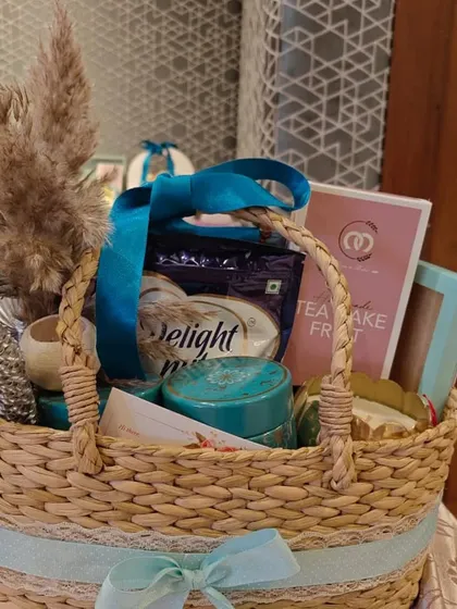 A special edition Diwali hamper in a woven basket, featuring a blue and white theme with a tea cake and other curated items.