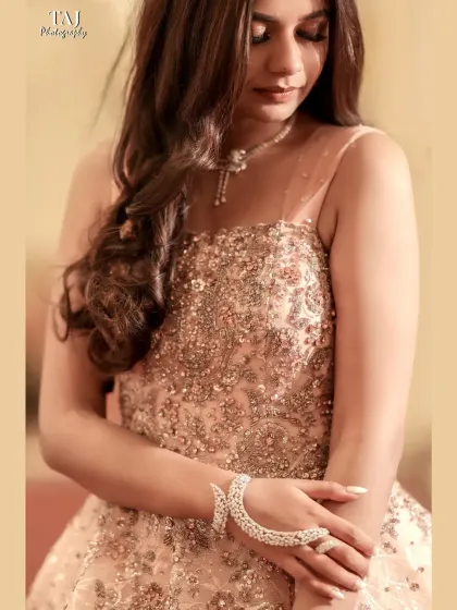 A delicate and detailed shot of the bride in a beautiful peach gown. The focus is on the intricate beadwork and her elegant hand jewelry.