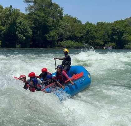 A raft hits a wave, sending water splashing and a participant leaning back in excitement.
