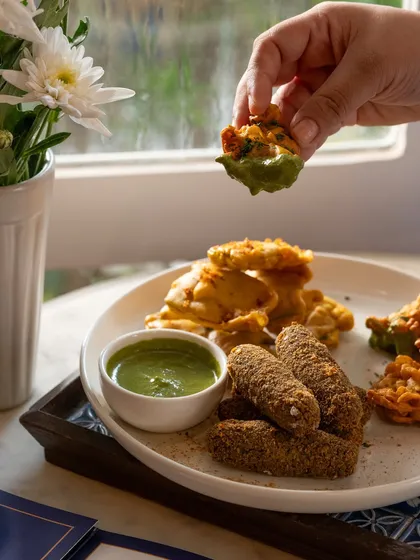 A plate of assorted pakoras with green chutney. The action of dipping a pakora makes the shot engaging and appetizing.