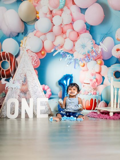 The aftermath of a successful cake smash! This little one is covered in blue frosting and pure happiness, surrounded by a festive donut-themed first birthday backdrop.
