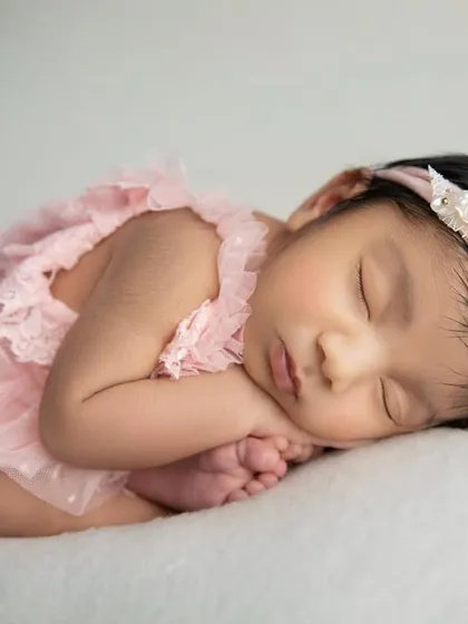 A classic side lying pose on a soft white blanket. The baby's pink outfit adds a beautiful pop of color.
