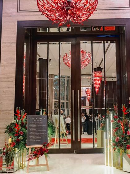 A modern and moody entrance for a reception. The design features dramatic red chandeliers, mirrored doors, and bold crimson floral arrangements, setting a tone of contemporary glamour.