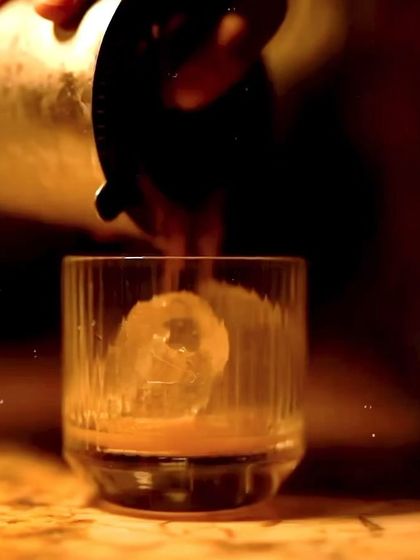 A classic cocktail being poured over a large ice cube, captured in a warm, moody light. This was part of a Christmas-themed event.