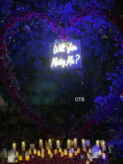 The complete proposal setup at night. The combination of the floral heart, neon sign, and dozens of electric candles on the ground creates an incredibly romantic and private atmosphere.