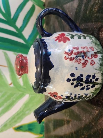 A close up of a hand painted ceramic teapot with a floral design, showcasing the detailed artistry our guests can achieve.