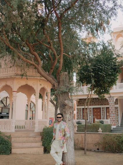 The groom looking cool and relaxed, leaning against a tree in the palace grounds during the Haldi festivities.