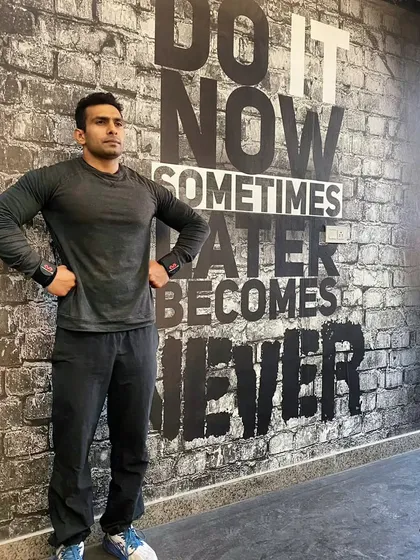 In front of our "Do It Now" wall. This is the mindset we encourage. Procrastination is the enemy of progress in fitness.