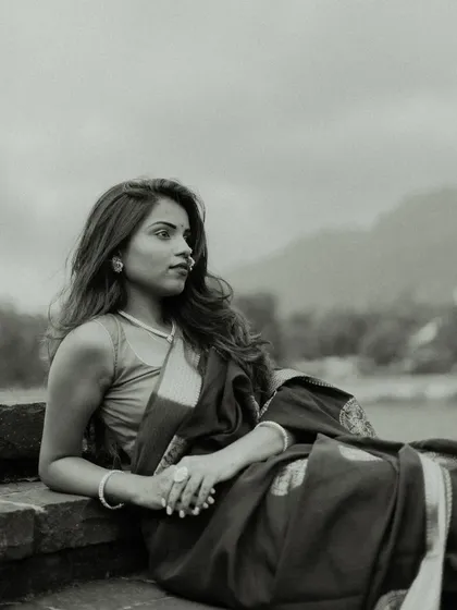 A pensive black and white portrait. The model is seated, looking out towards the horizon, with the landscape in the background adding a sense of scale and contemplation to the image.