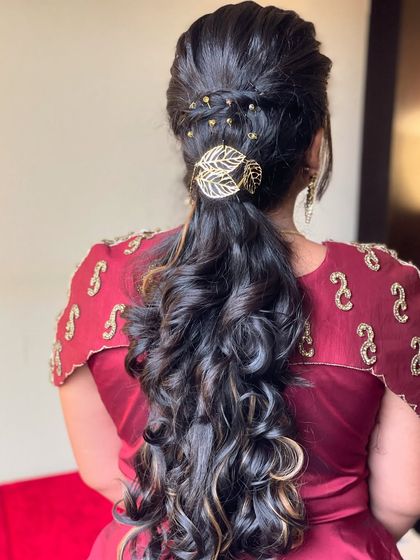 A modern and chic ponytail hairstyle with voluminous curls. This look is perfect for a reception or party, and is accented with a delicate, leaf-patterned hair clip.