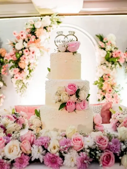 A wedding cake should be as magical as the love story it celebrates. This three-tiered buttercream cake, adorned with fresh pink and white roses and a custom "Mr & Mrs" topper, was the centerpiece of a beautiful floral-themed reception.