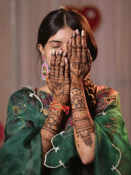 A shy bride peeking through her beautifully adorned hands. The intricate mehandi design adds to her bridal charm.