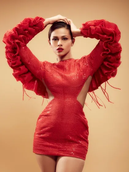 A full-length shot showcasing a powerful, high-fashion makeup look with a classic red lip. The makeup provides a strong focal point that complements the voluminous red gown, creating a cohesive and striking editorial image.
