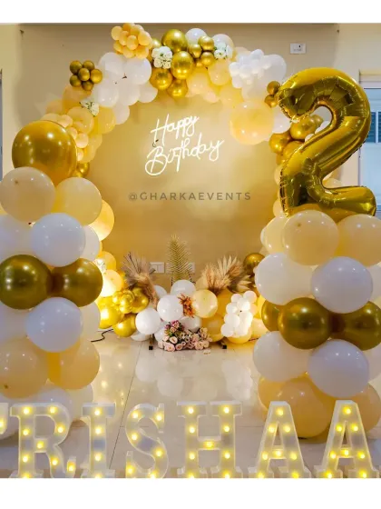 A beautiful gold and white balloon arch for Trishaan's 2nd birthday, with a neon sign and marquee letters.