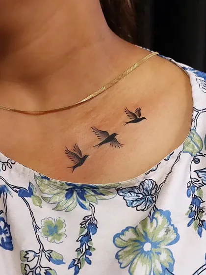 Three small birds in flight on the collarbone, symbolizing freedom and journey. The clean silhouettes make for a timeless and elegant minimalist tattoo.