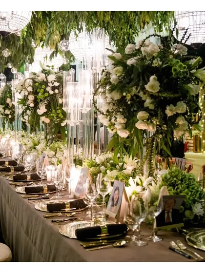 A breathtaking view of a long dining table under a canopy of greenery and hanging lanterns, perfect for a sophisticated evening celebration.