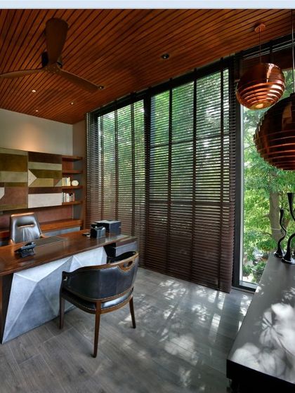 Sunlight filters through wooden blinds into the study, creating a calm and productive atmosphere. The design balances privacy with a strong visual connection to the lush garden just beyond the glass walls.
