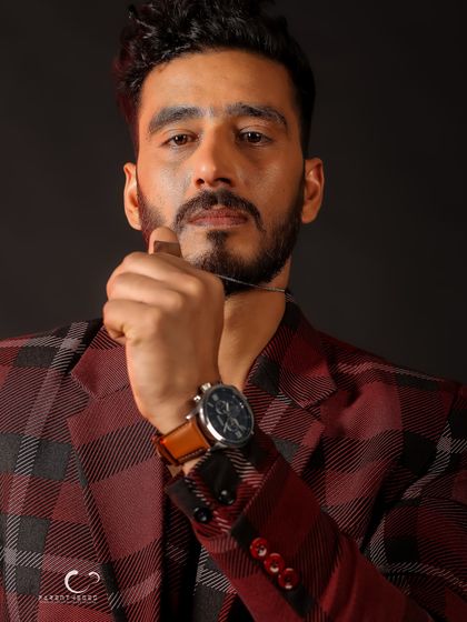 A close-up shot focusing on intensity and detail. The way he holds the necklace draws attention to his face and the subtle accessories.