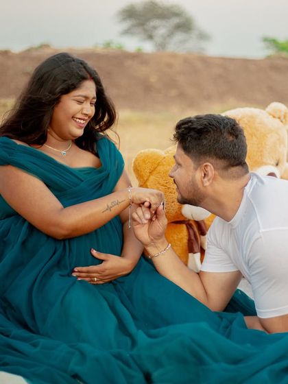 A playful and loving moment during a maternity picnic shoot. The flowing teal gown adds a touch of elegance to this casual and happy scene.
