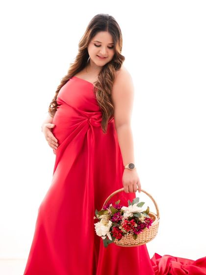 A vision in red. This mother-to-be holds a basket of flowers, her flowing red gown creating a striking contrast against the minimalist white background. It's a simple yet powerful fine art portrait.
